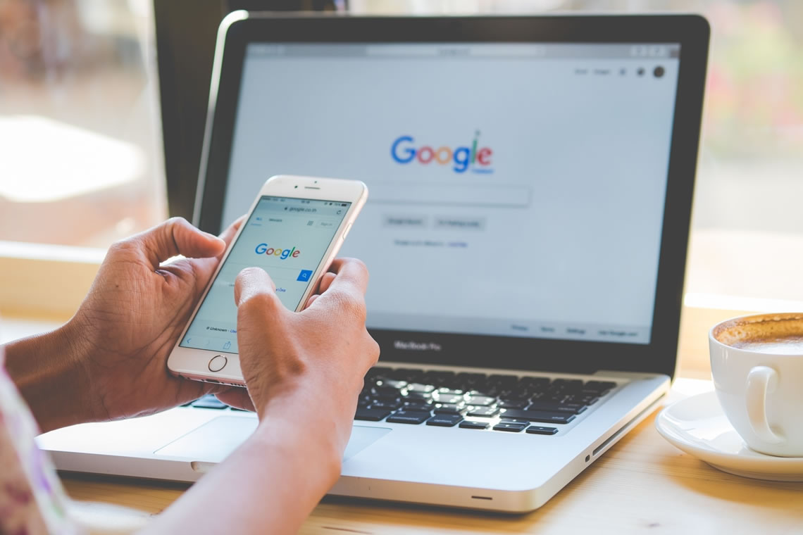 person using google on iphone and laptop at his desk with cup of coffee